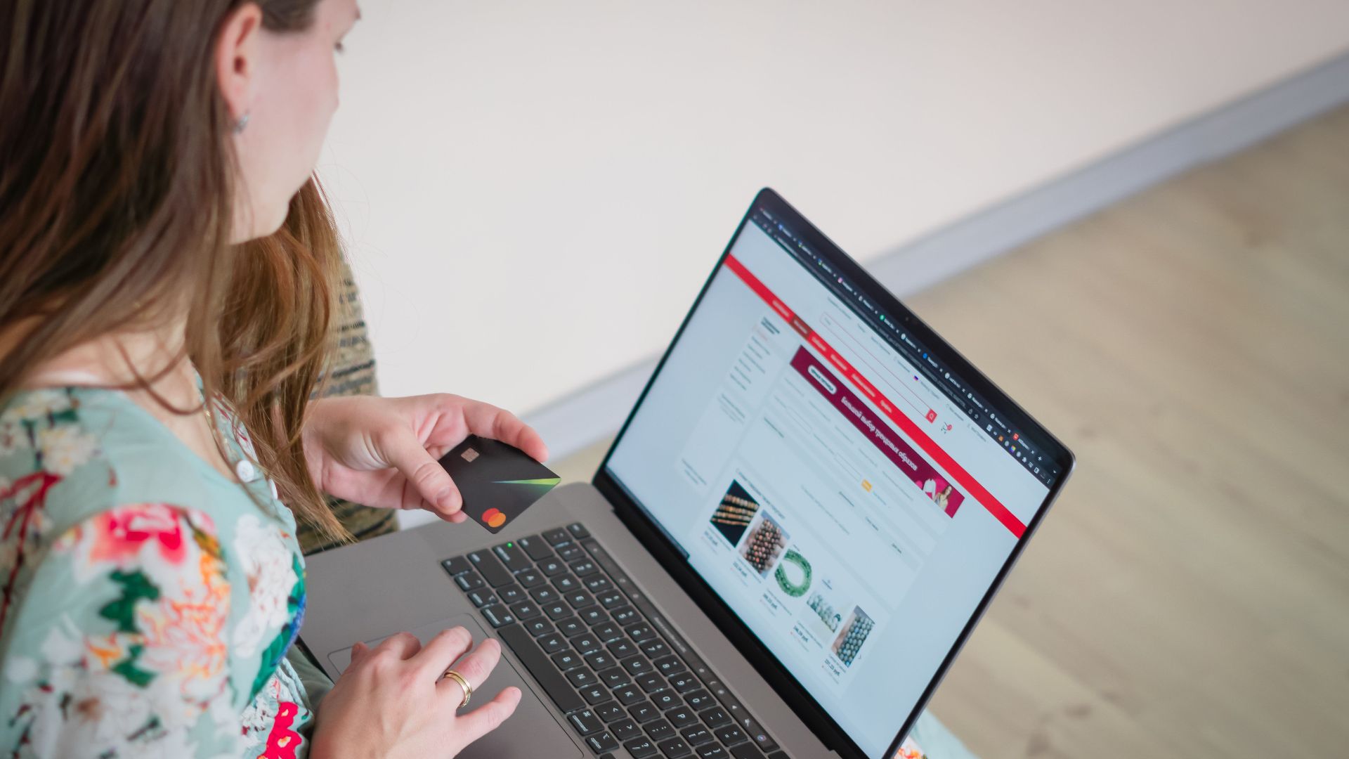 Woman in floral dress shopping online with a laptop and credit card indoors.