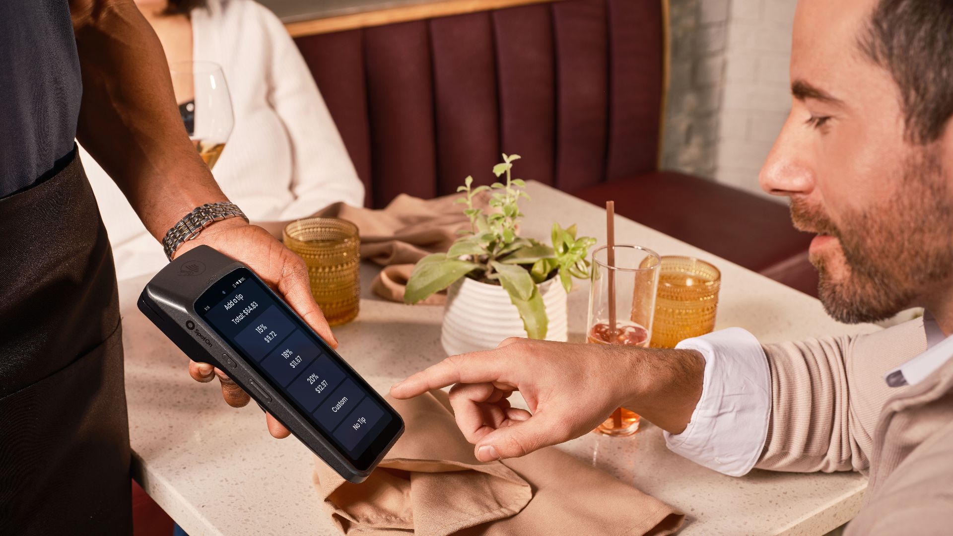 A diner uses a handheld POS system for digital tipping in a casual restaurant setting.