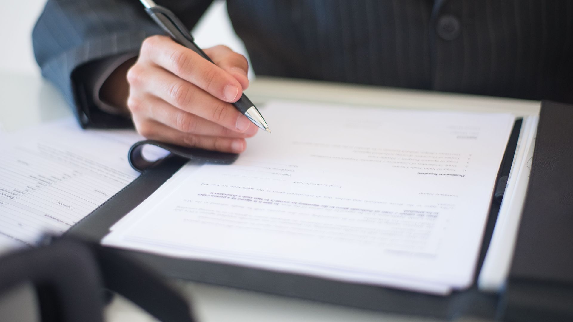 Close-up of a hand signing documents with a pen, symbolizing an important business contract.
