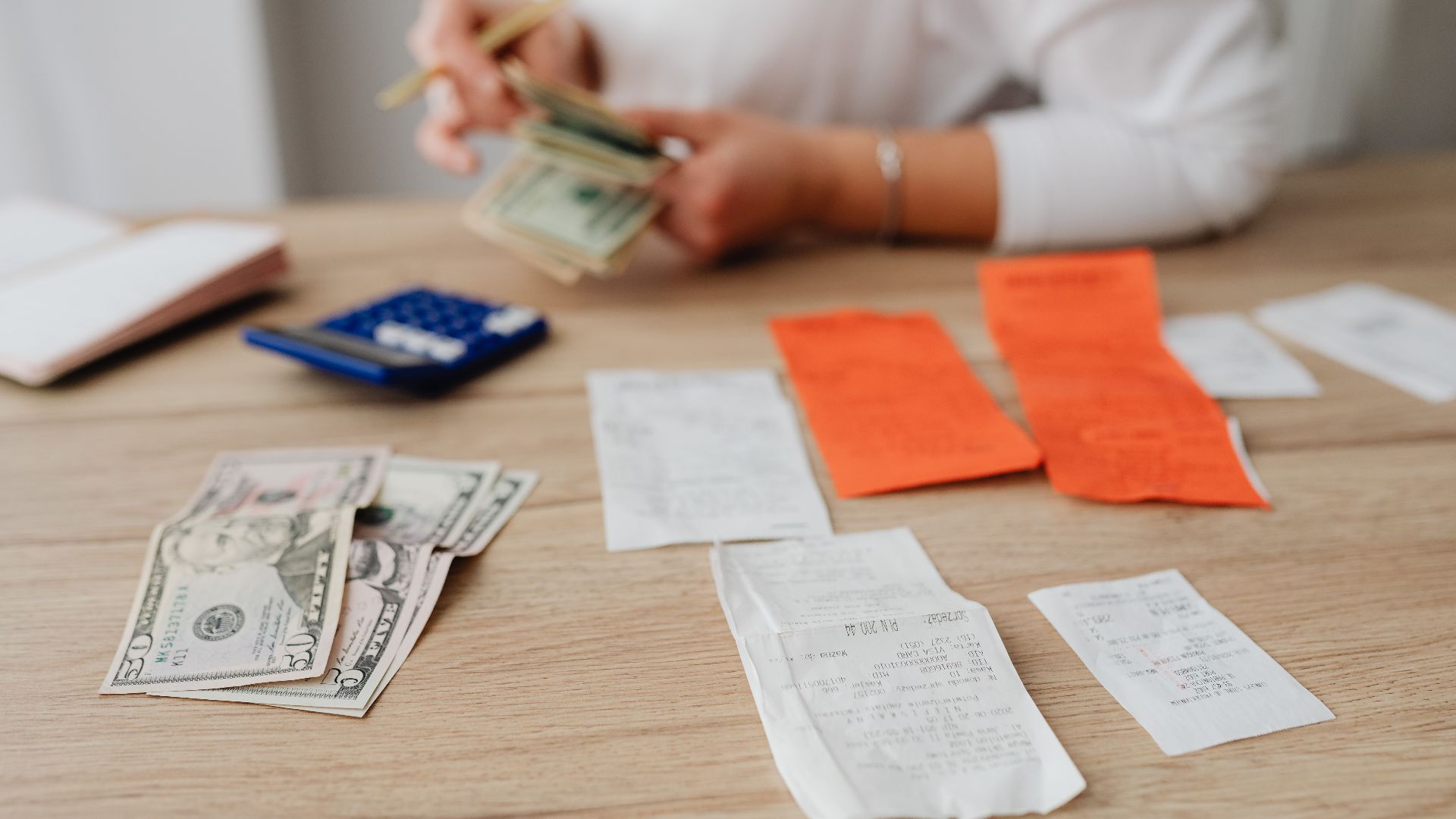 A person using a calculator and cash to plan a household budget.
