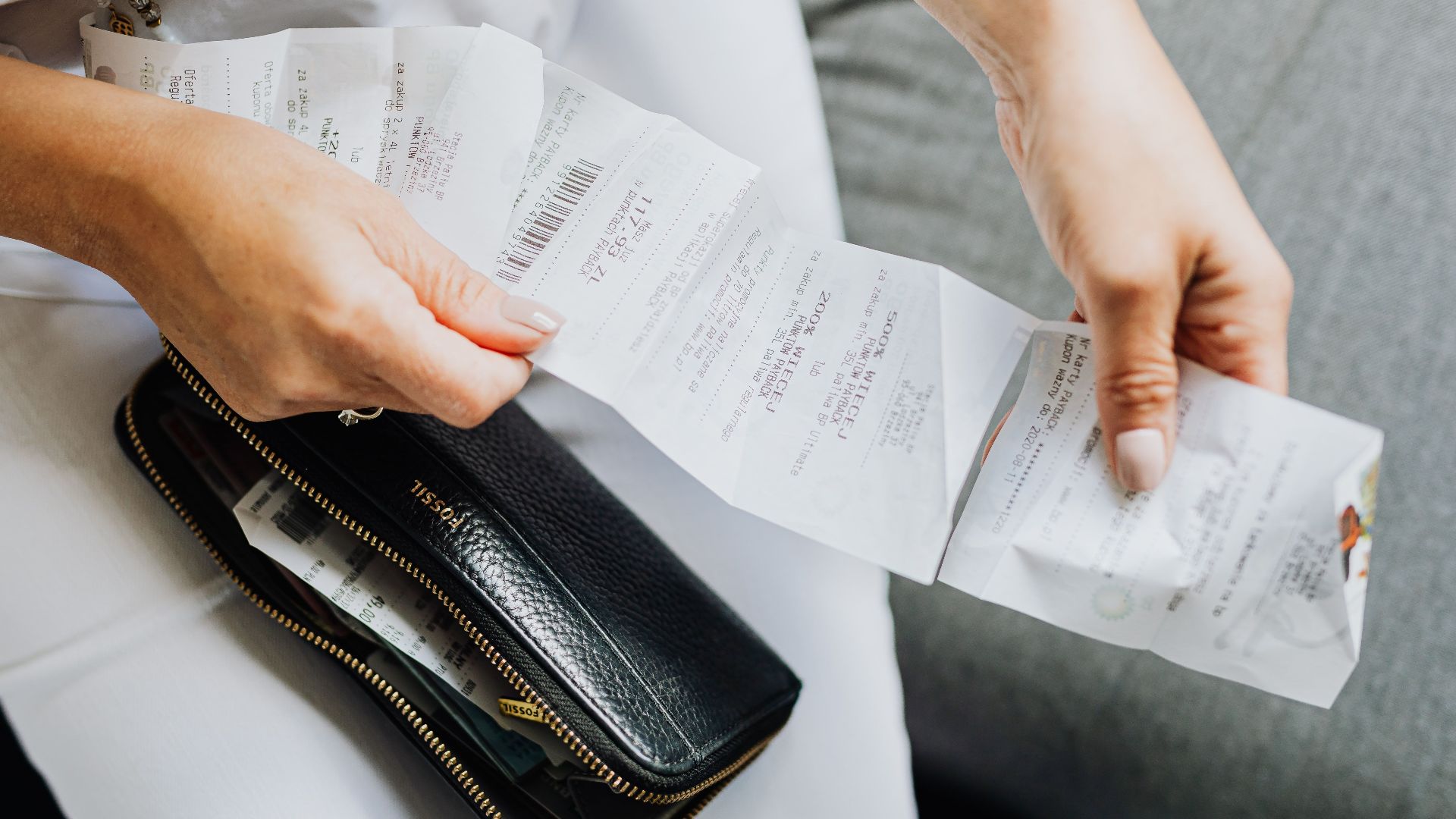 Close-up of a woman's hands managing multiple receipts taken from a black wallet.