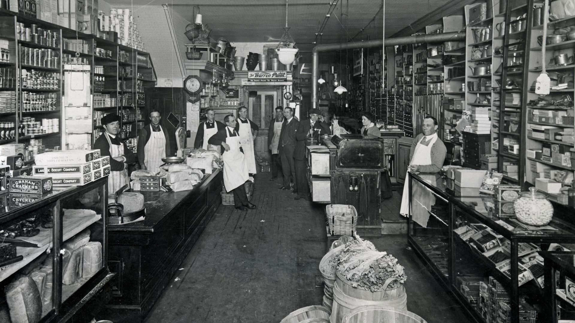 A black and white photograph of employees and customers as they pose for a photo inside the Rodemich Brothers grocery store on Miami Street in the East Toledo area of Toledo, Ohio. The brothers advertised themselves as