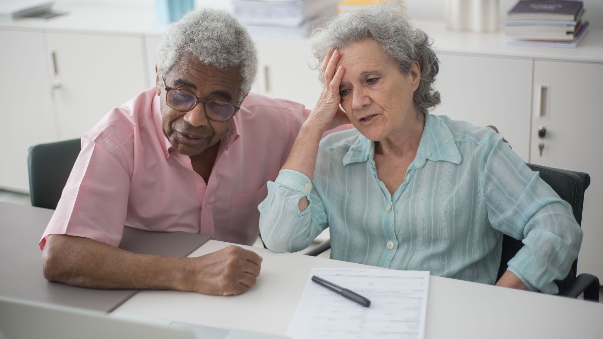 Elderly couple engaged with a laptop, reviewing paperwork at home office desk.