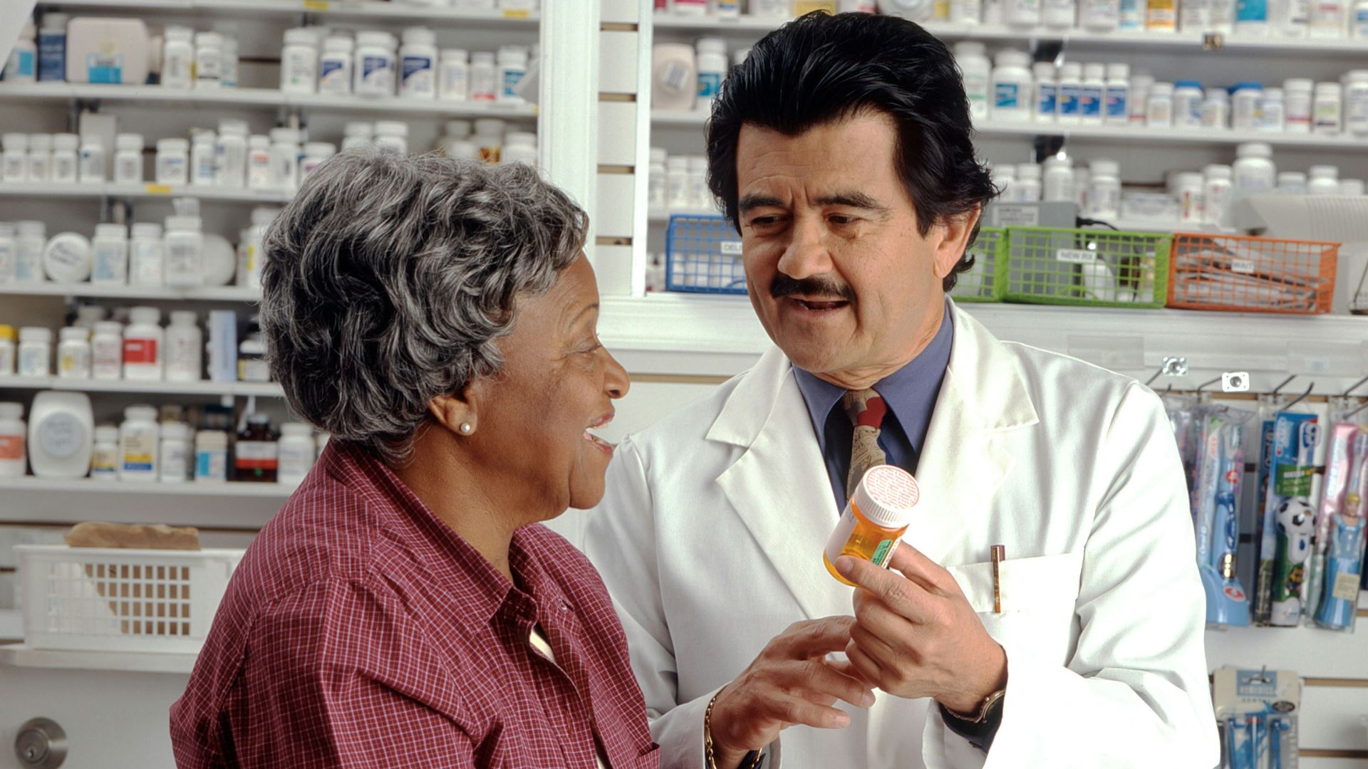 A pharmacist in a white coat showing a pill bottle to a woman