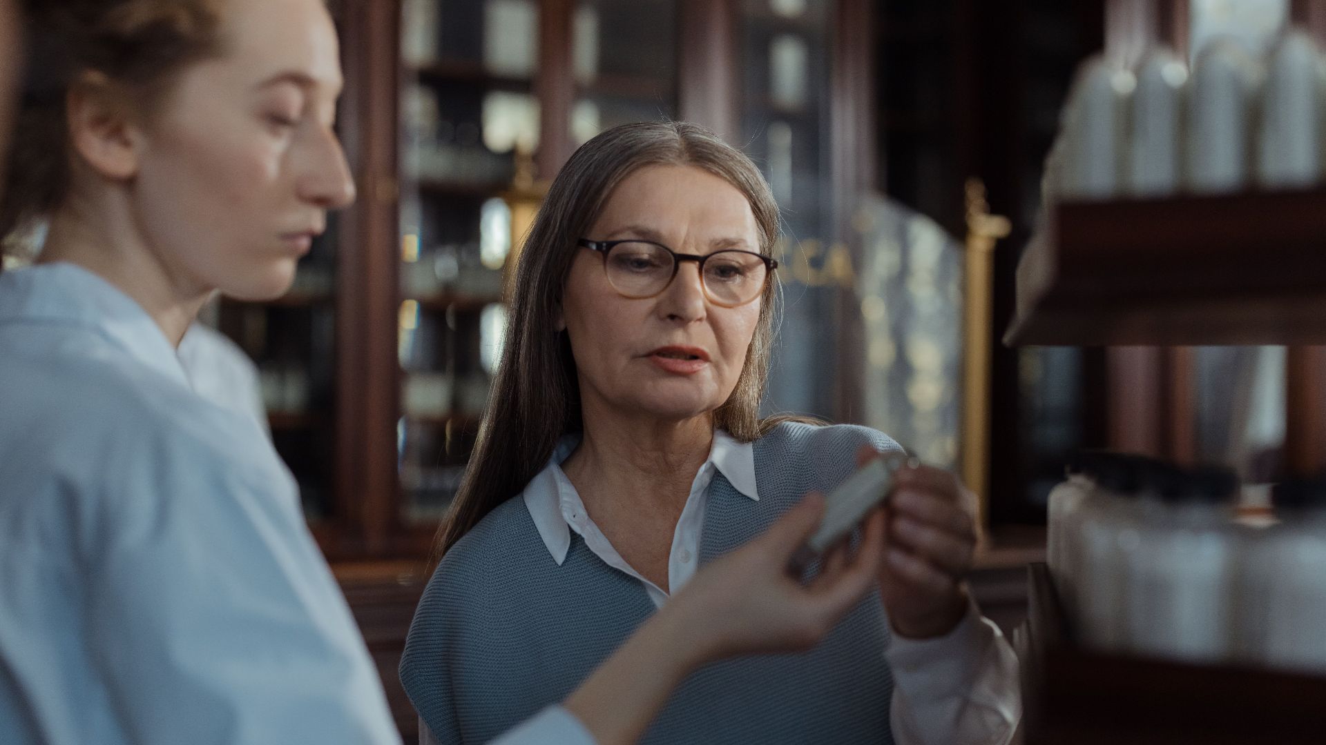 An elderly woman discussing medication options with a pharmacist at a pharmacy counter.