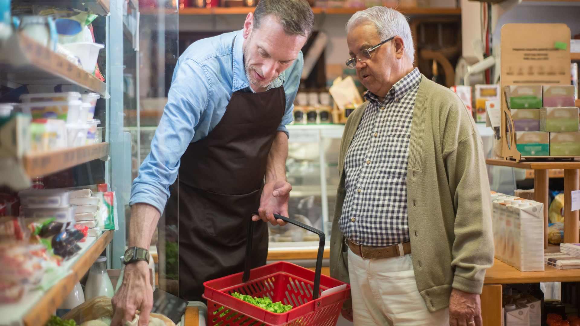 A salesman helps an elderly man with shopping in a local grocery store.