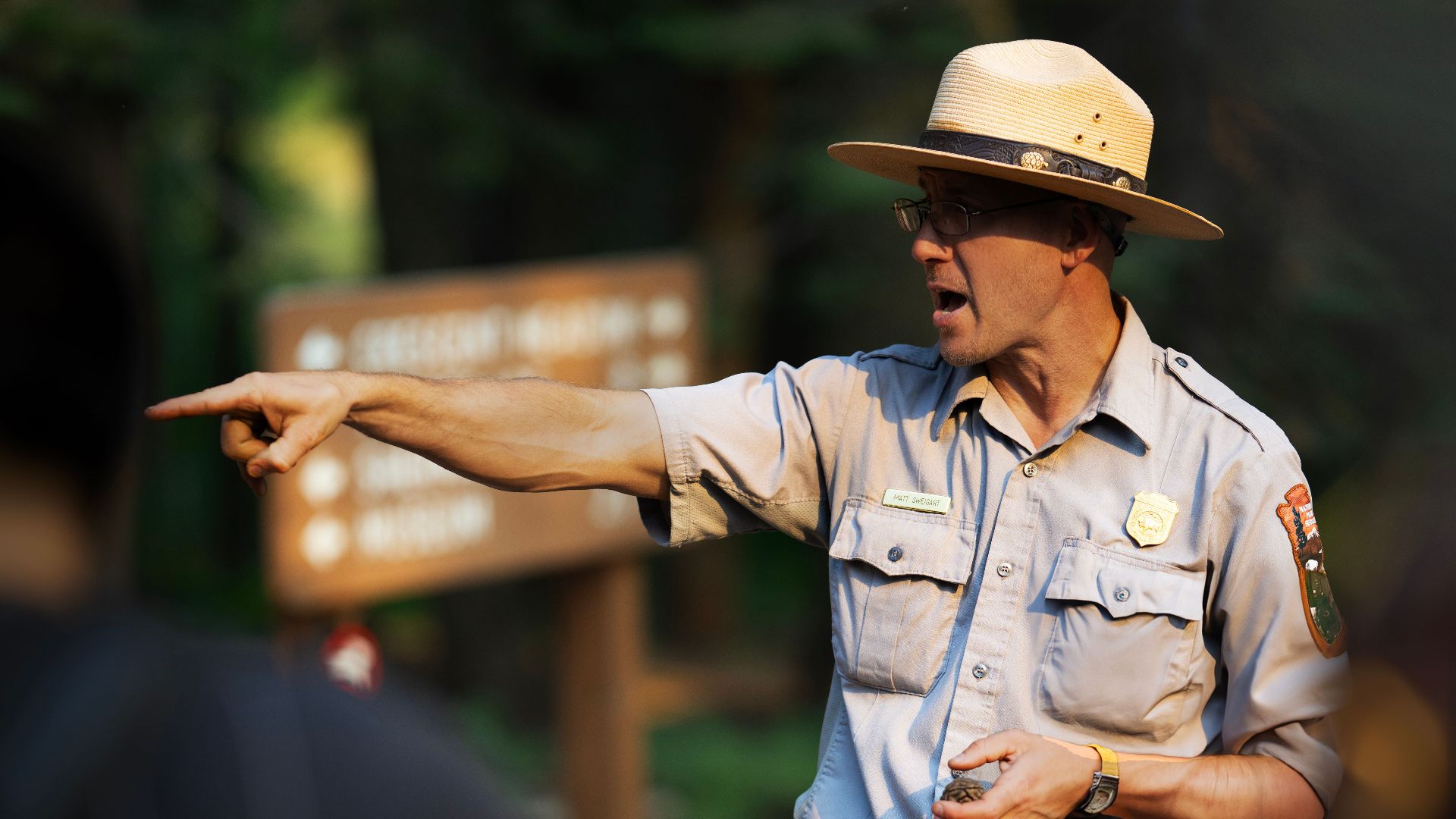 Park ranger guiding a group through a forest area, pointing with emphasis.