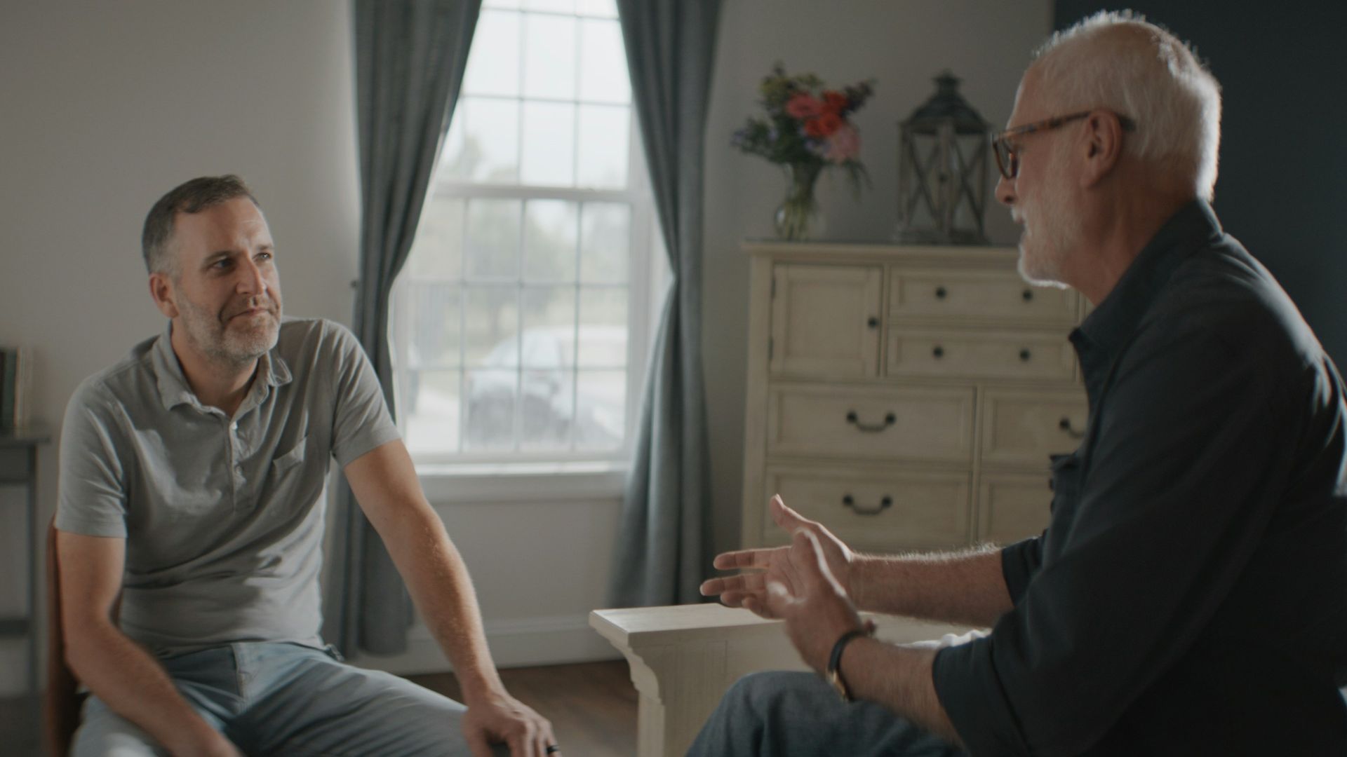 Two men talking in a sunlit room