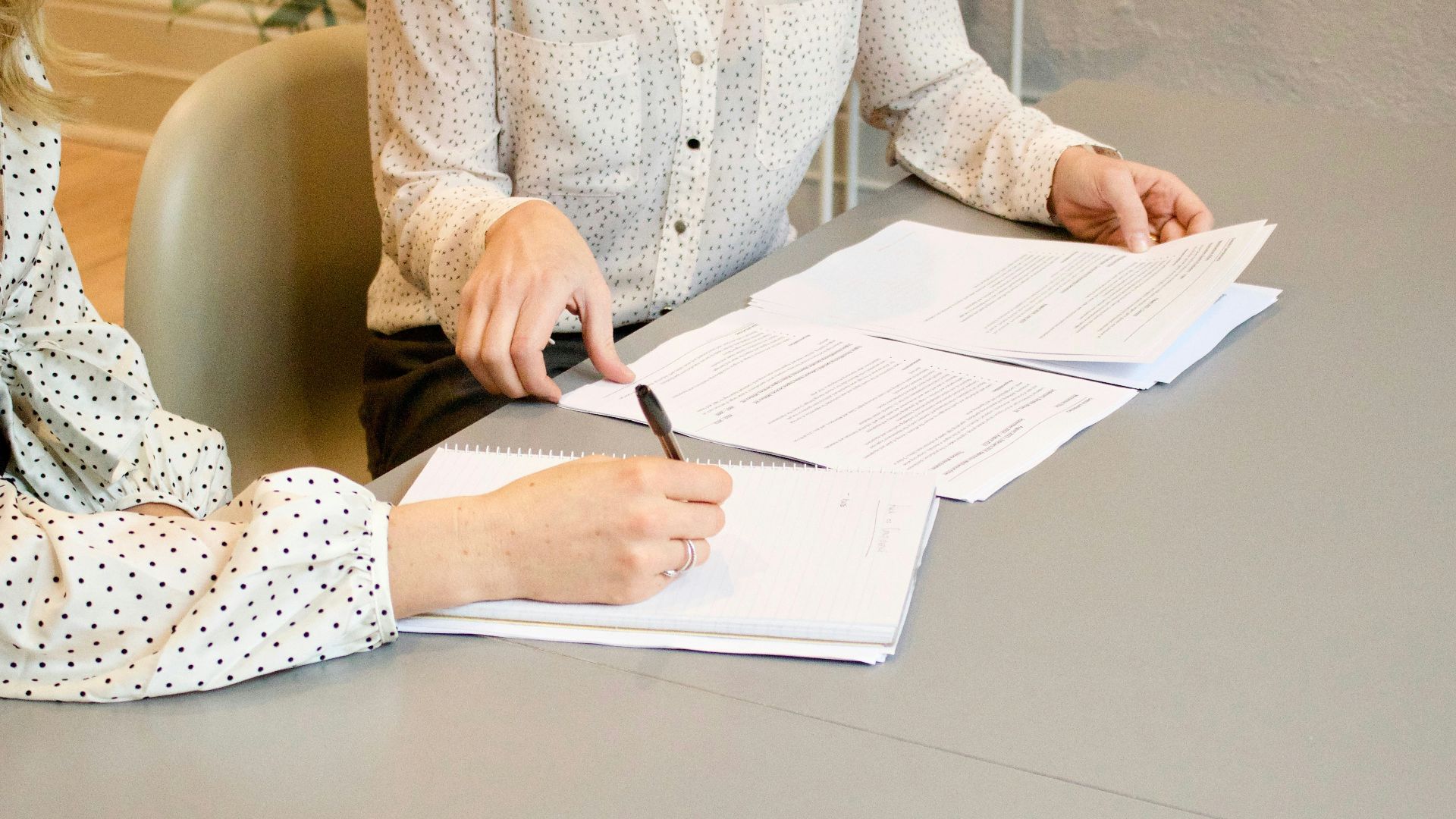 woman signing on white printer paper beside woman about to touch the documents