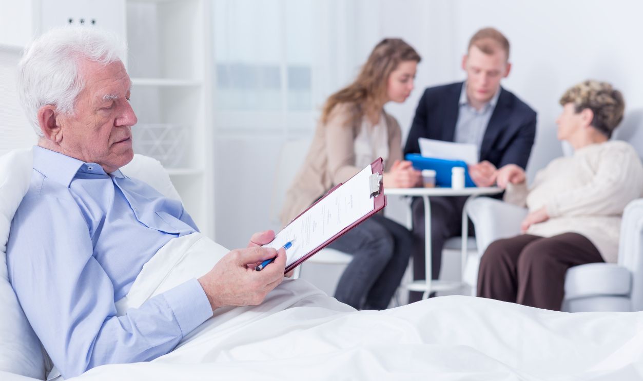 Elderly man in a hospital bed analysing the documents he is about to sign, with his family in the blurred background