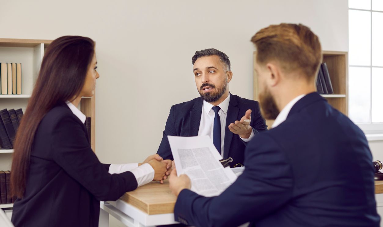 Family lawyer in suit speaking to clients. Couple sitting at desk, reading divorce settlement agreement, consulting with law expert, listening to him answer questions, and getting help with paperwork