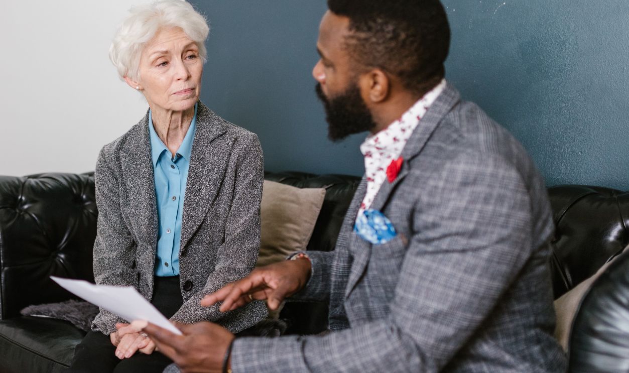 An elderly woman and a man in a professional meeting discussing documents indoors