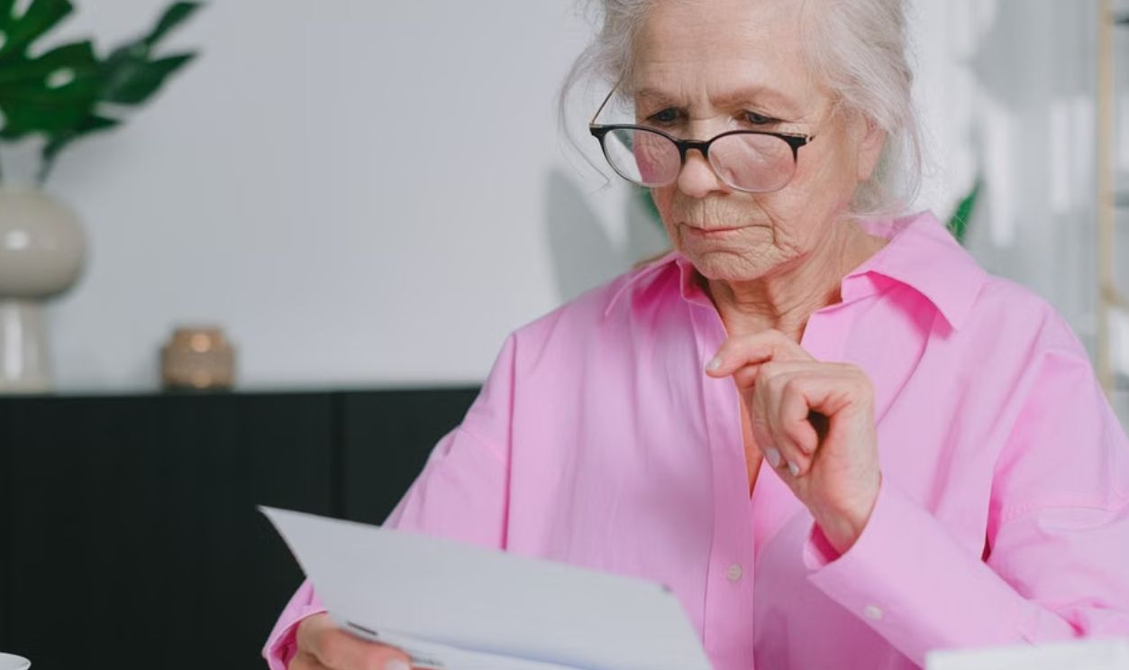 Elderly woman in pink shirt reading documents at home workspace