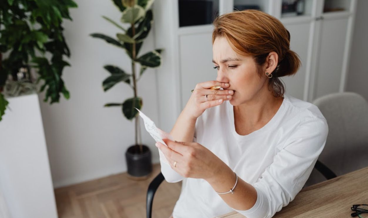 Pensive woman in home office analyzing documents at her desk, surrounded by plants.
