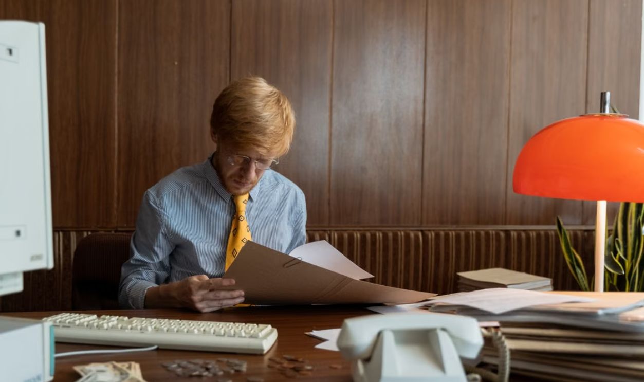 Man in retro office setting reviewing documents under warm light. Ideal for business themes.