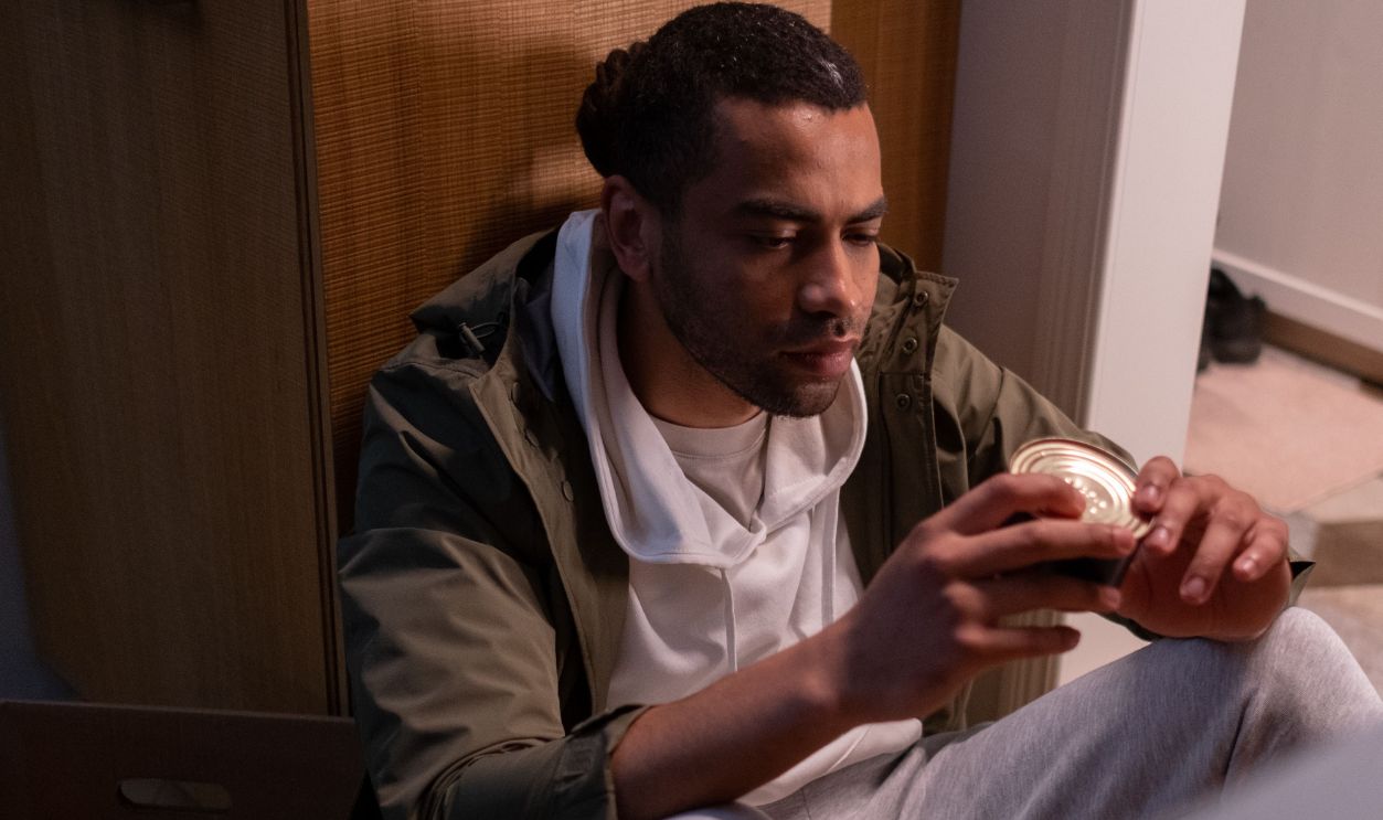 A man sits quietly in his kitchen holding a canned good
