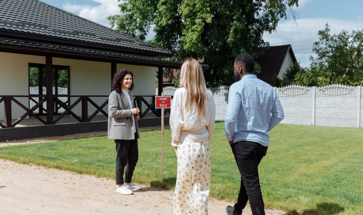 A diverse group viewing a house for sale with a real estate agent outdoors