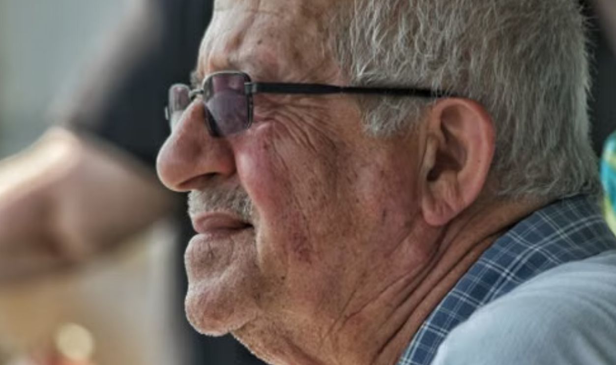 A senior man wearing sunglasses smiles outdoors, capturing a moment of joy and reflection