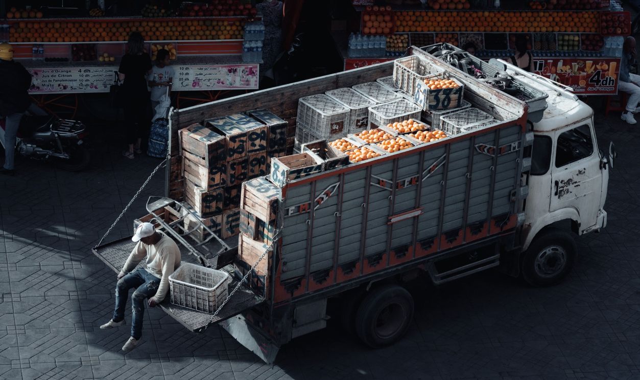 A truck loaded with crates of oranges parked at an urban market scene
