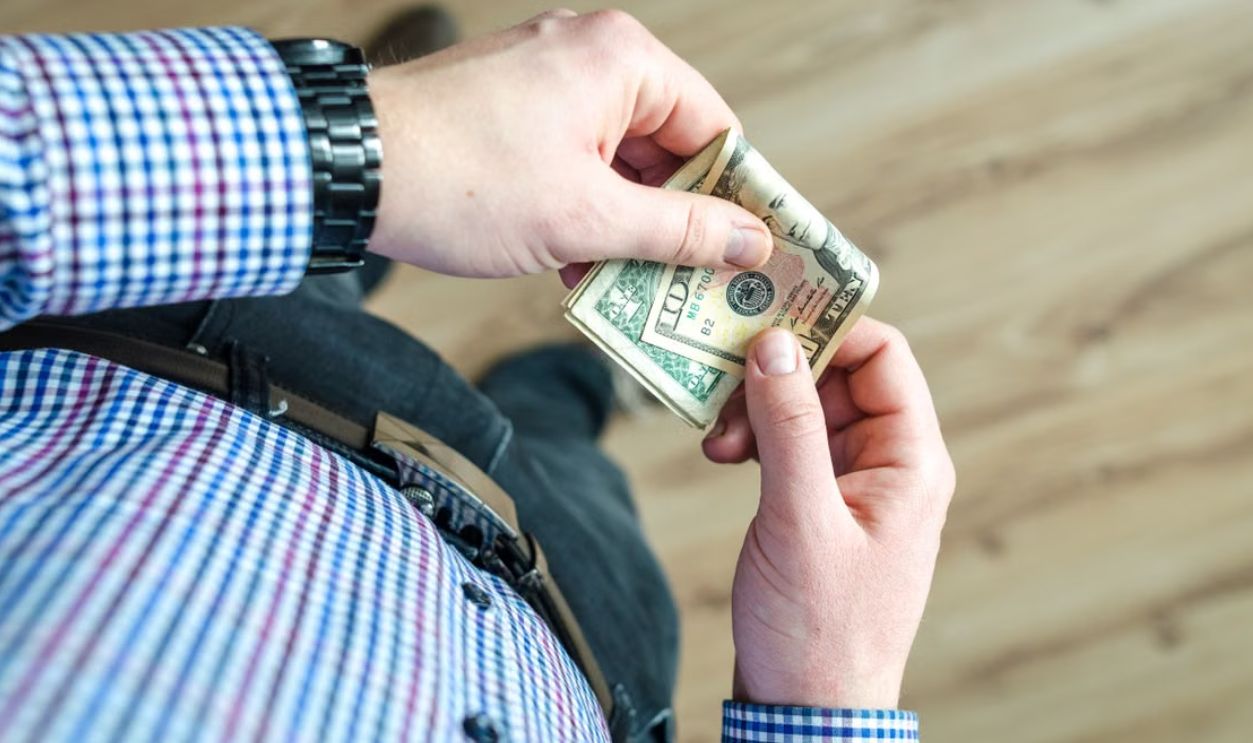 Close-up view of a man in casual clothes holding US dollar bills in his hands.