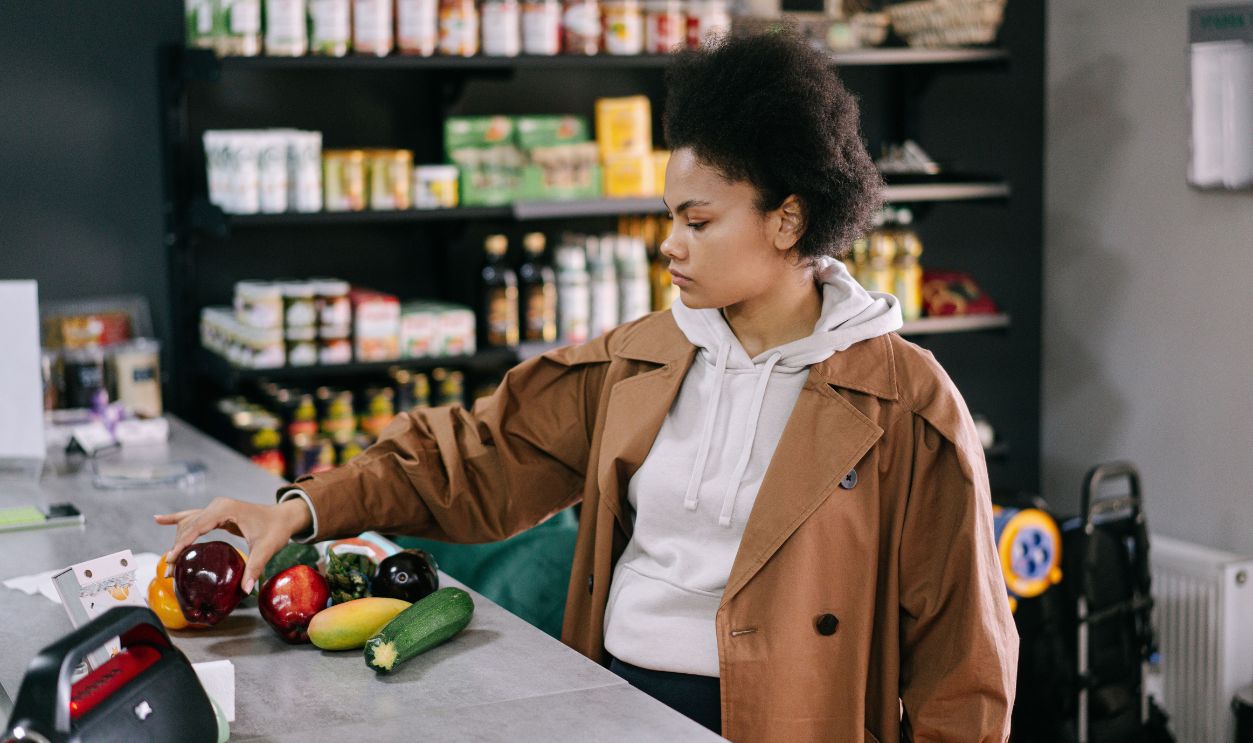 A woman selecting fresh fruits and vegetables at a grocery store with shelves