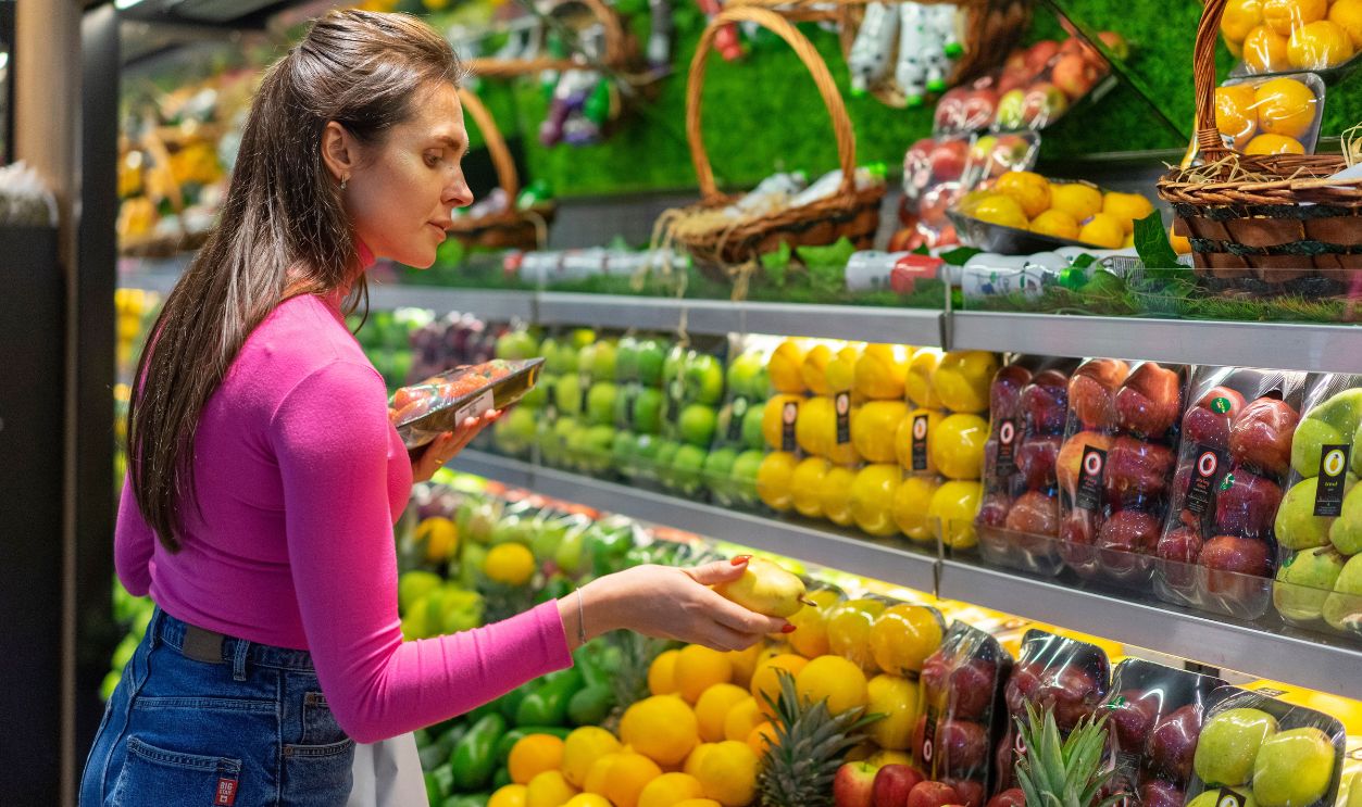 A woman examines fresh fruits in a vibrant grocery store produce section, shopping