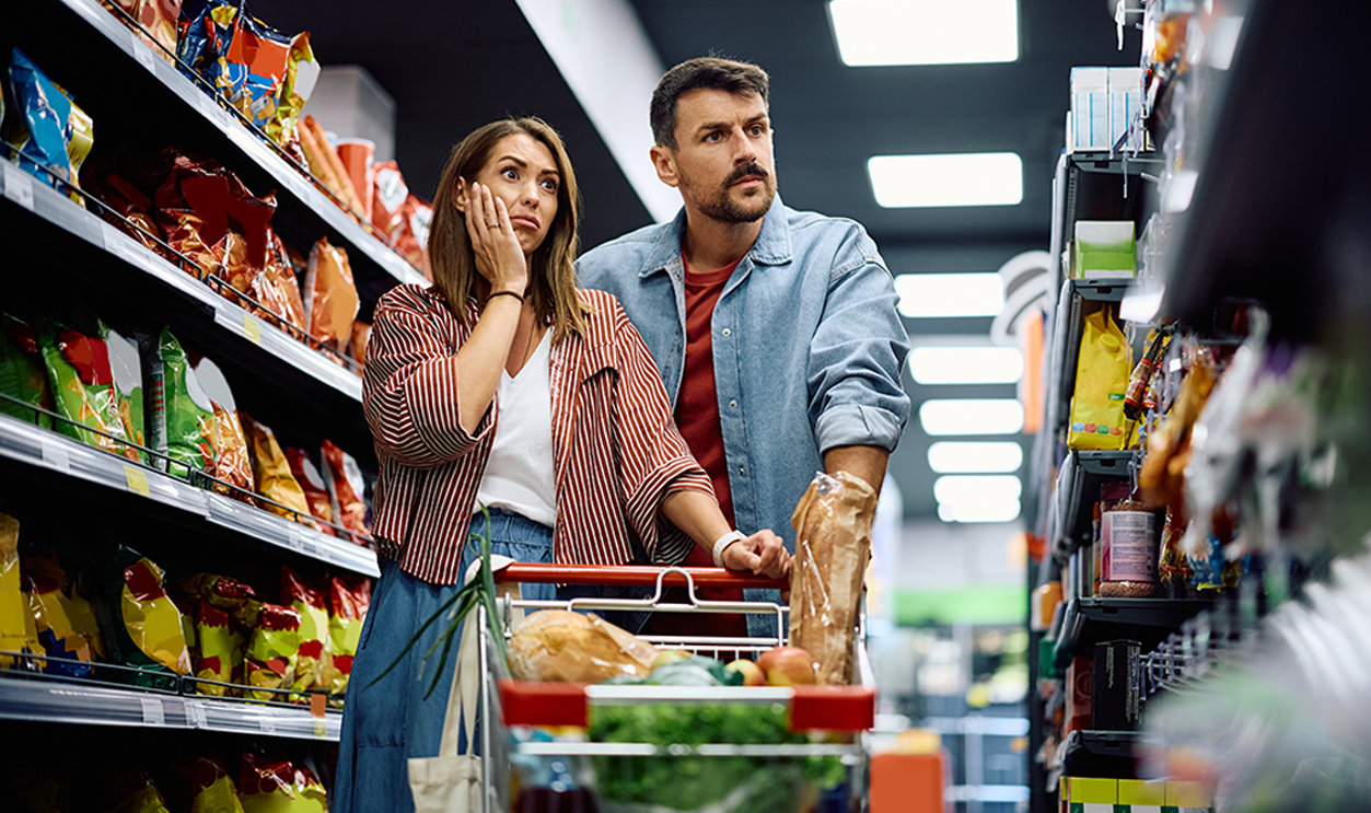 Shocked couple looking at grocery shelf in disbelief