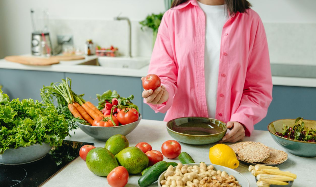 Woman in pink overshirt holds tomato in kitchen with fresh fruits