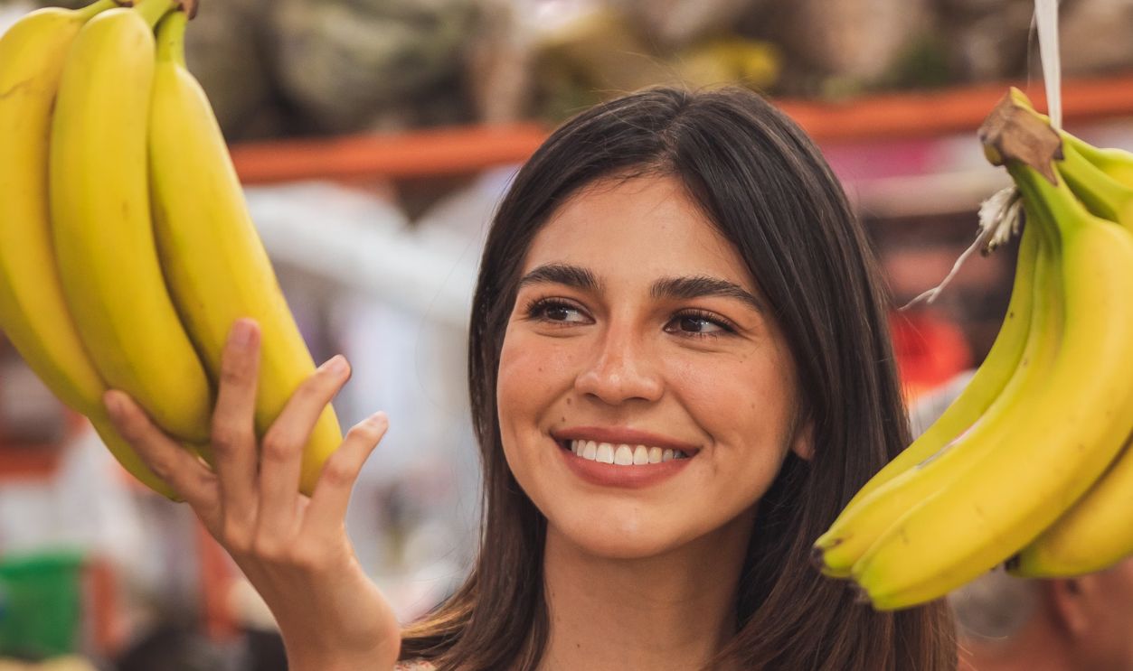 Woman enjoying shopping for bananas at a vibrant indoor market. Capturing the joy of fresh produce