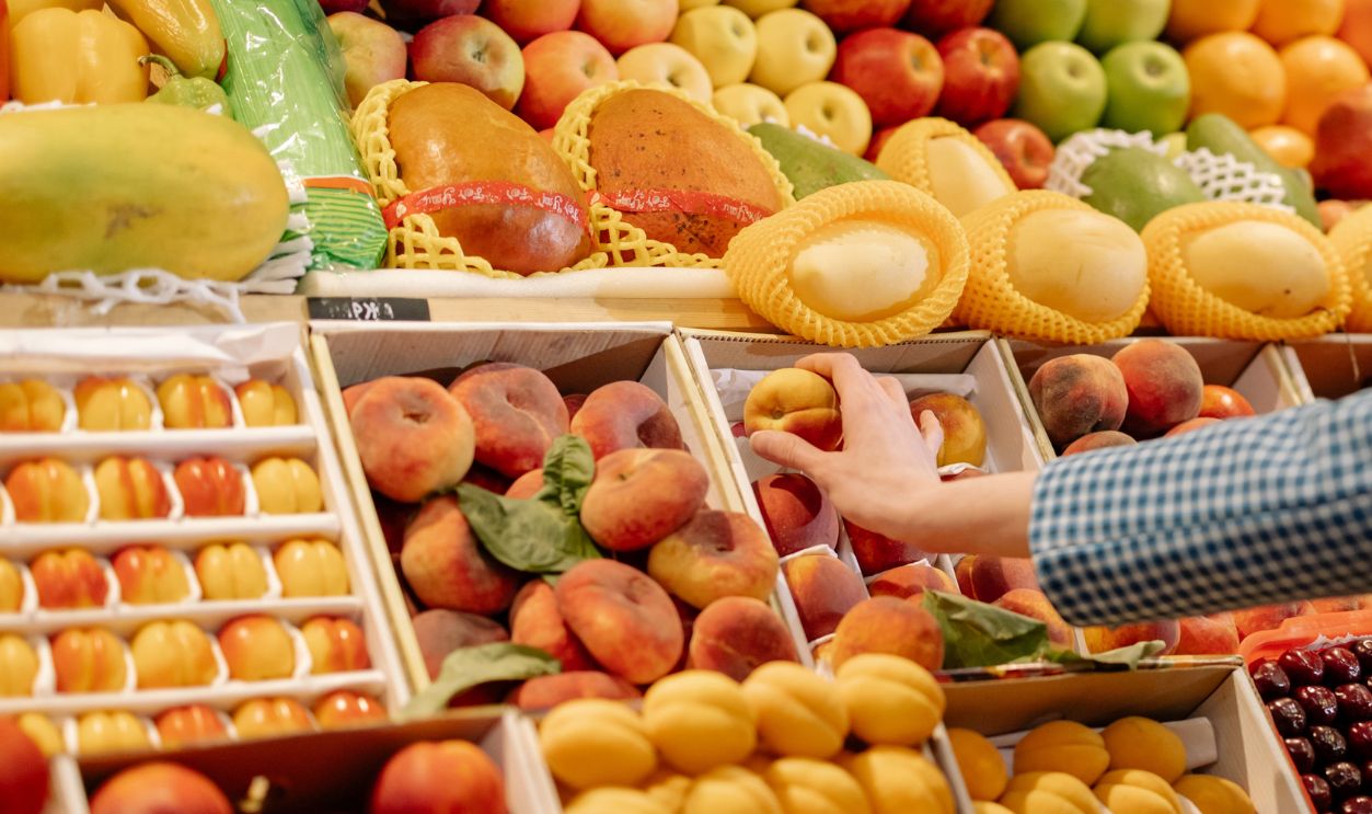 A colorful variety of fresh fruits at a market stand with a hand selecting a peach