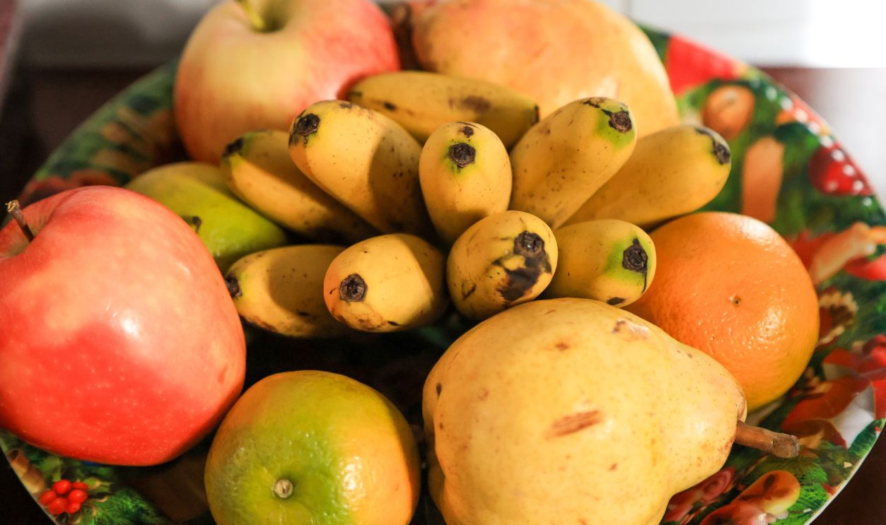 Vibrant still life of various fresh fruits like red apples, yellow pears, baby bananas, and citrus fruits displayed on a holiday-themed plate, perfect for healthy eating and nutrition concepts