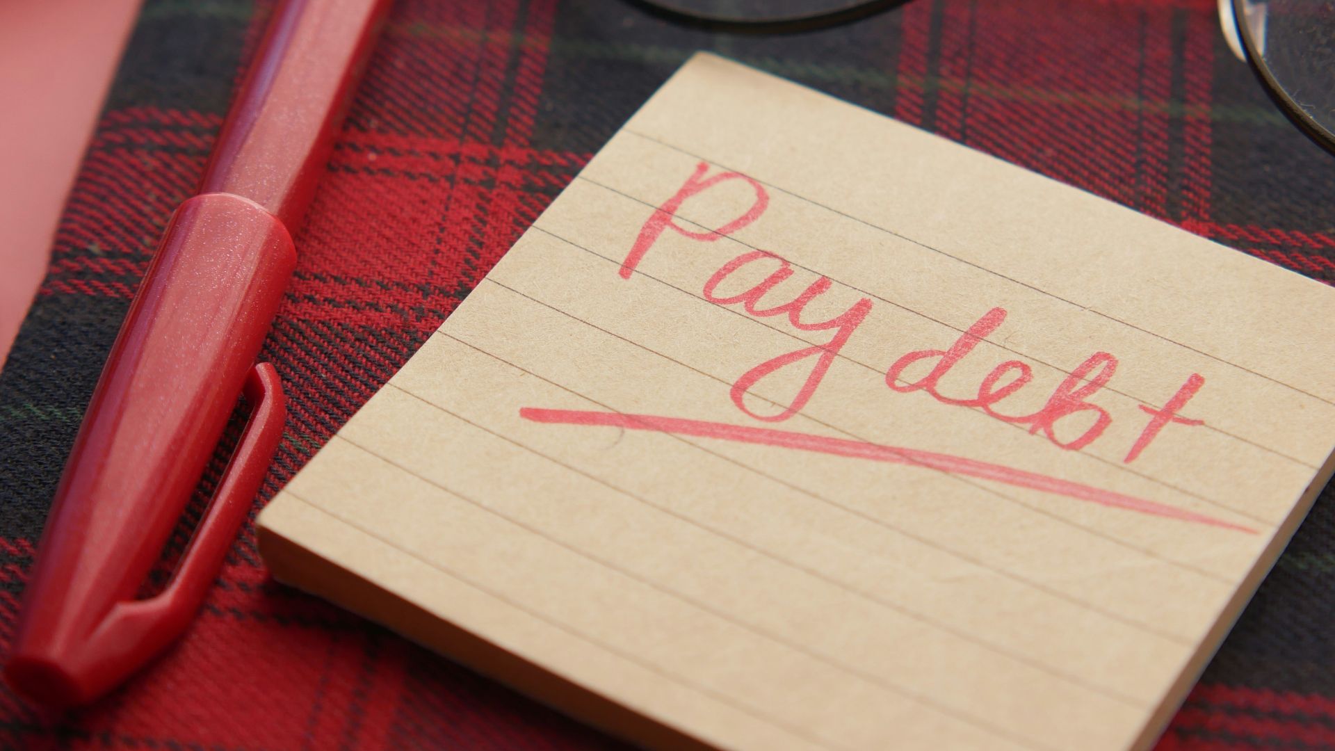 a note that says pay debt next to a pen and glasses