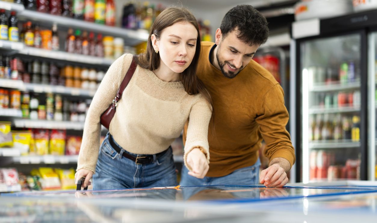 Young couple selecting frozen foods from freezer at supermarket