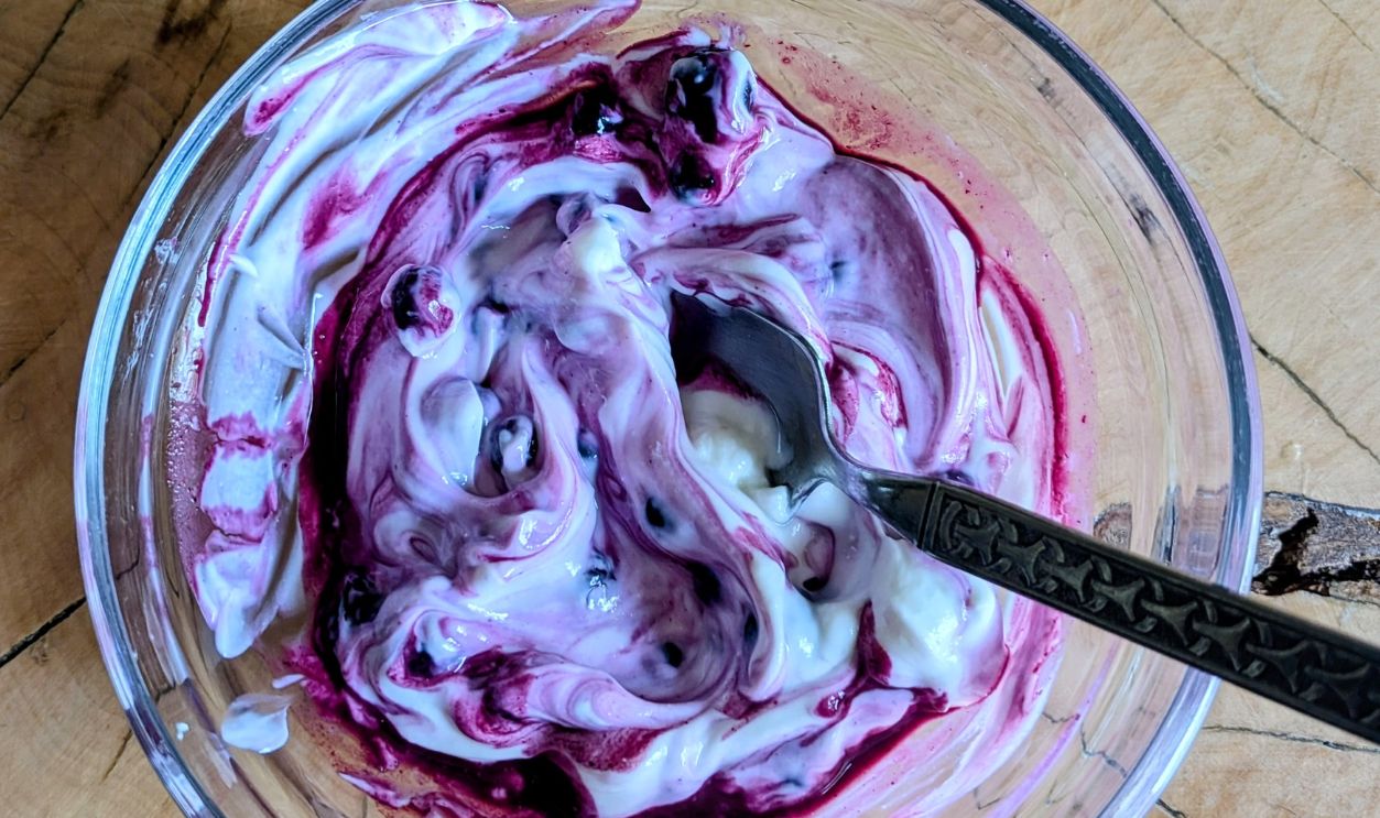 Top view of creamy yogurt with vibrant blueberry swirl in a glass bowl on rustic wooden table.