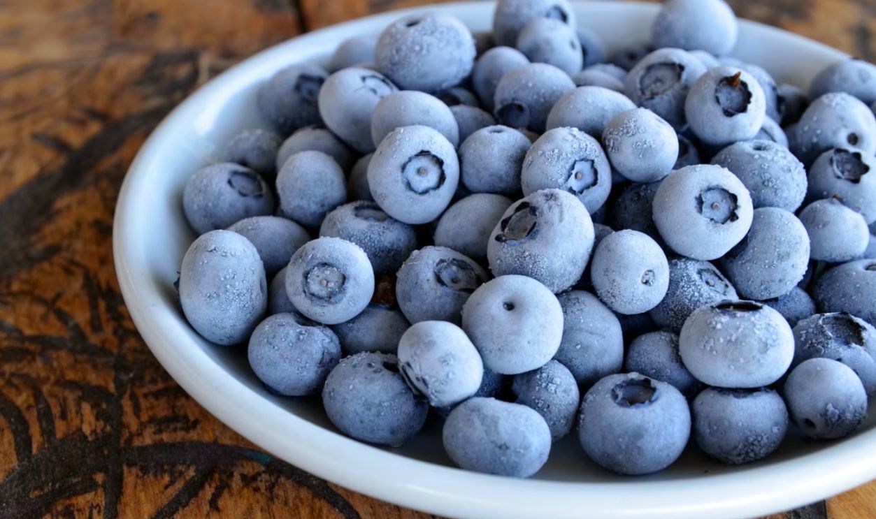 Close-up of frozen blueberries in a white bowl on a rustic wooden table, highlighting texture