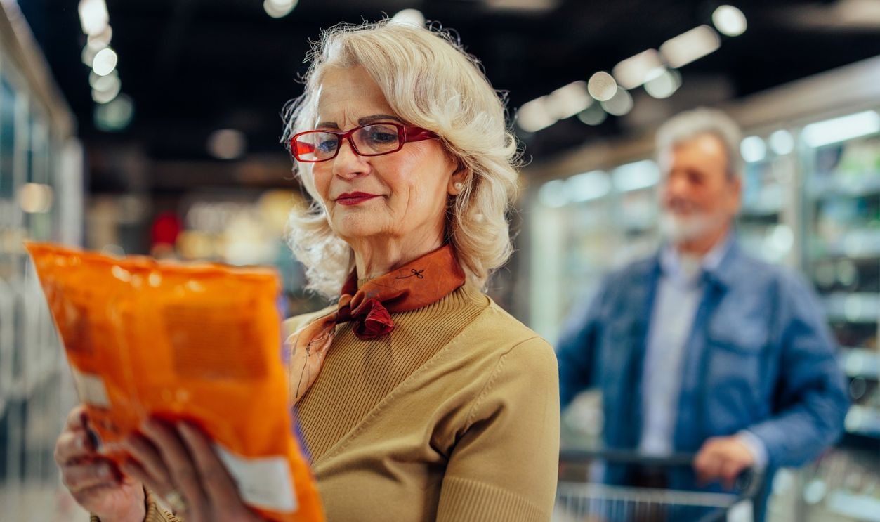 Smiling woman shopping in supermarket and reading product information.