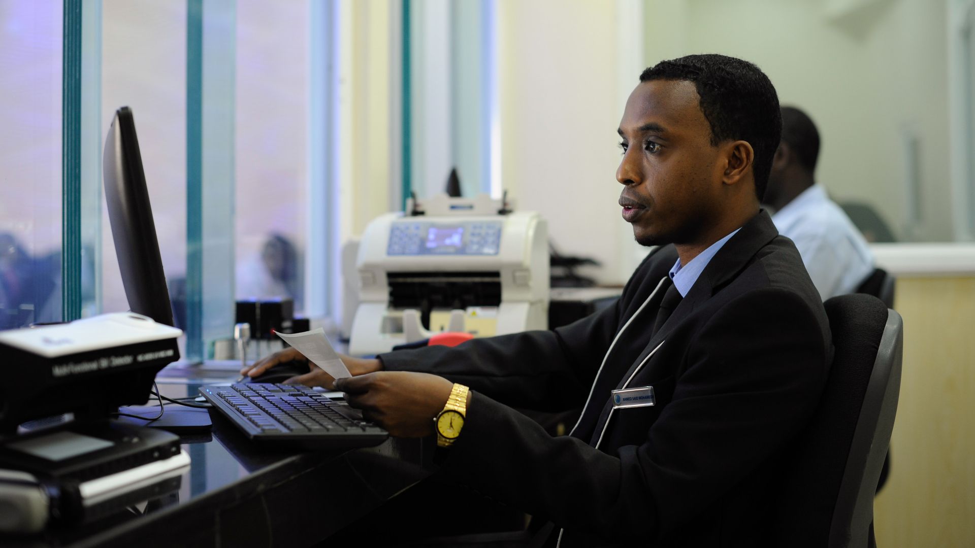 A teller fulfills a request from a customer. Rather than operating as a conventional bank, IBS operates under the Islamic banking code, a practice which seeks to be consistent with the principles of sharia. AMISOM Photo