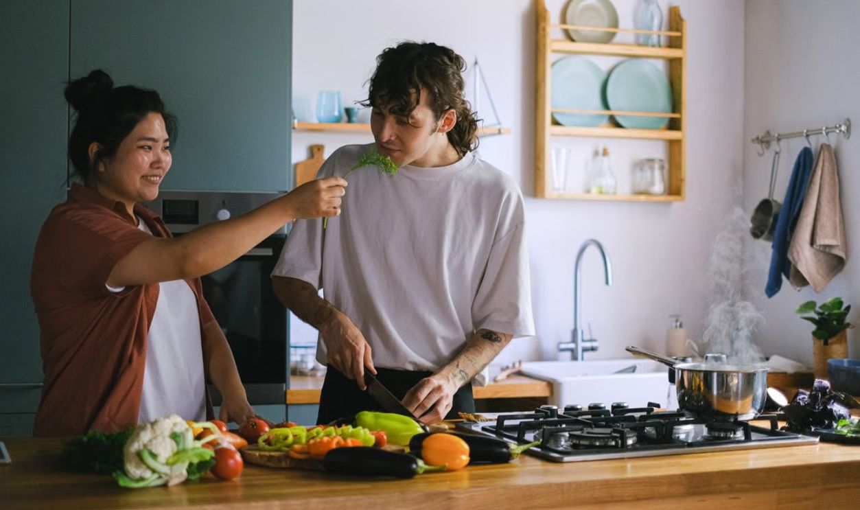 Two people preparing a meal together, surrounded by fresh vegetables in a warm kitchen setting.
