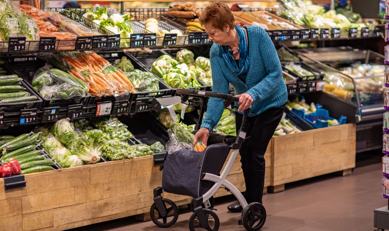Elderly woman using rollator walker while shopping for fresh vegetables