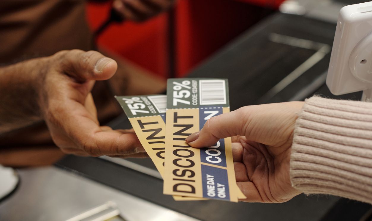 Closeup of unrecognizable female customer handing discount coupons to cashier at supermarket checkout line, copy space