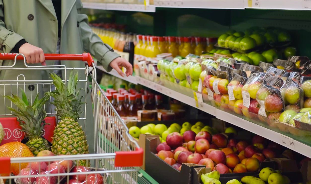 Woman shopping for groceries walking through the supermarket with a trolley. A woman shopper makes purchases, takes products from a shelf in a store.