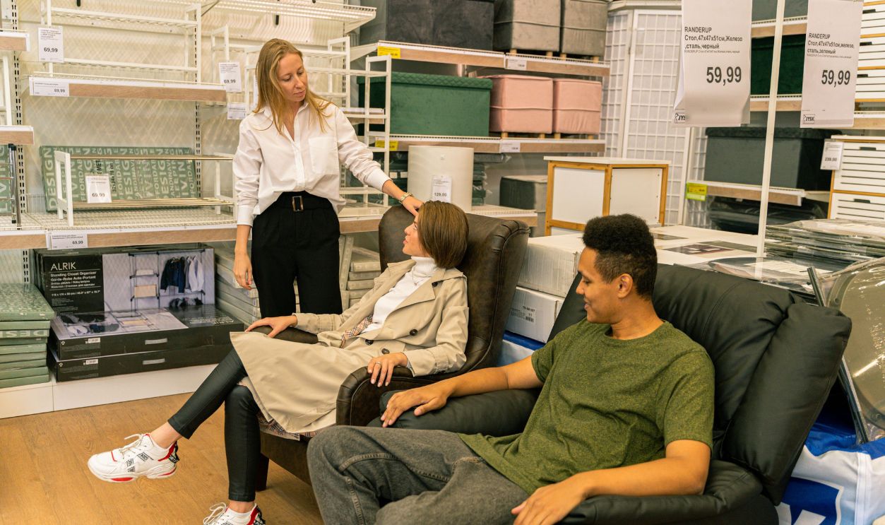 Shoppers try out leather chairs in a modern home furnishings store, guided by a salesperson