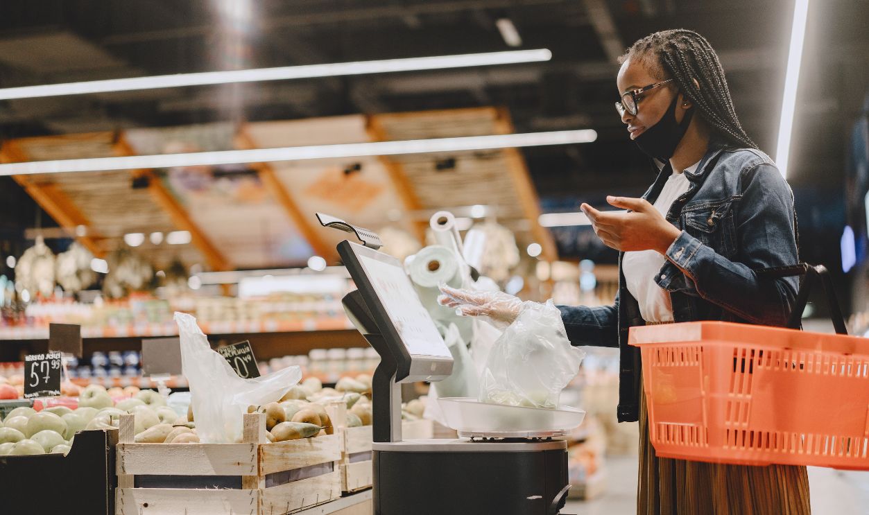 A woman with a mask shops and weighs groceries in a modern supermarket