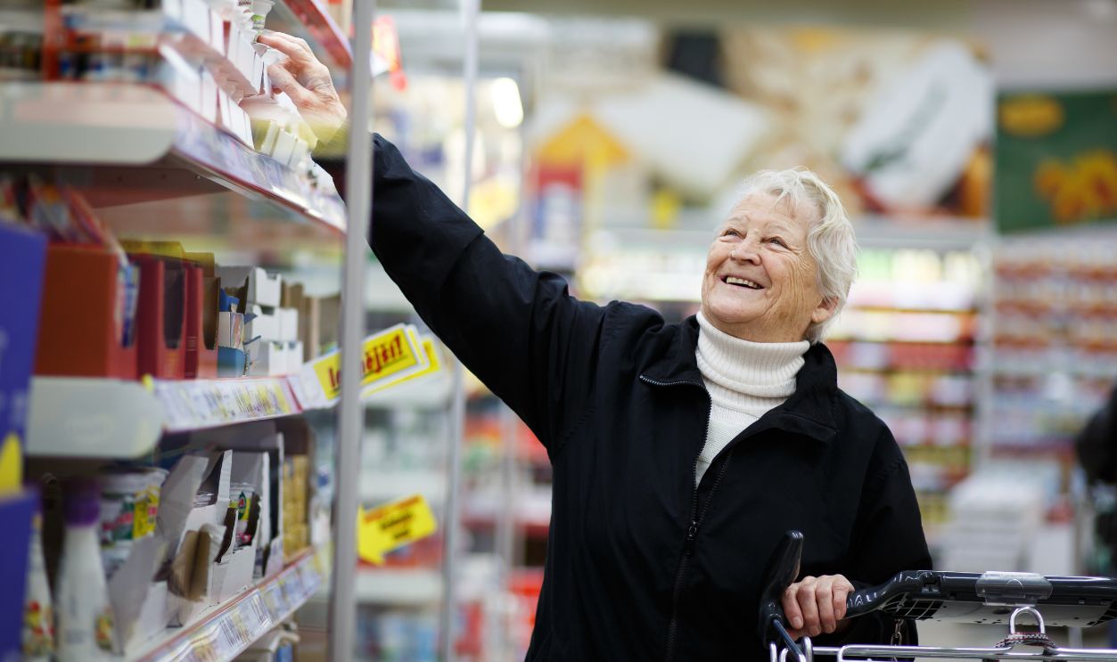 Elderly woman choosing dairy produce in supermarket, shopping for dairy produce in department of a grocery store/supermarket ( color toned image )