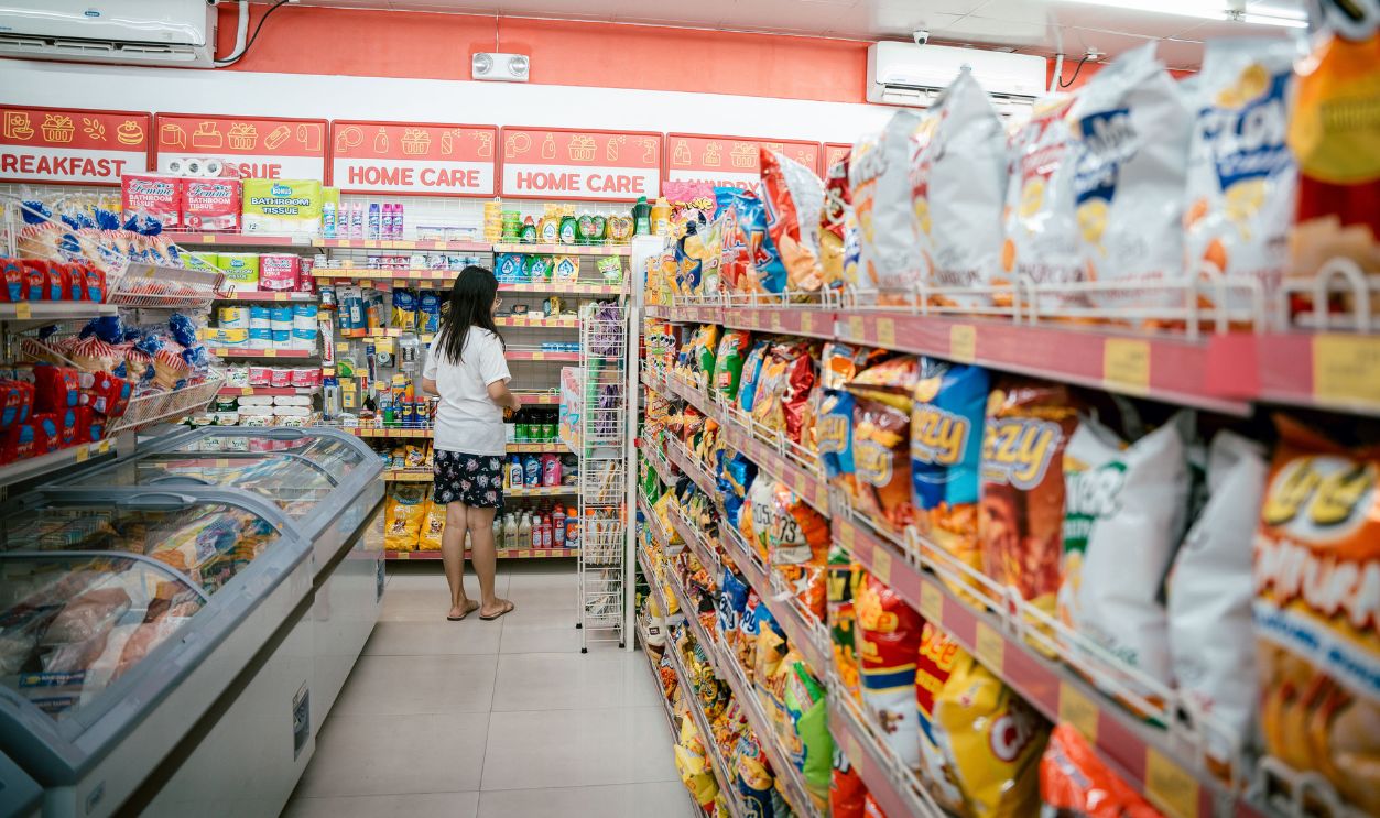 A woman browsing snack shelves at a supermarket, surrounded by various chips
