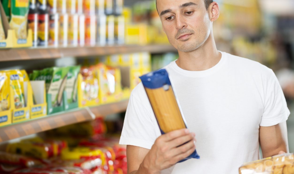 Man near department display of pasta in hypermarket. Buyer chooses between variation of noodles, considers various options, compare items