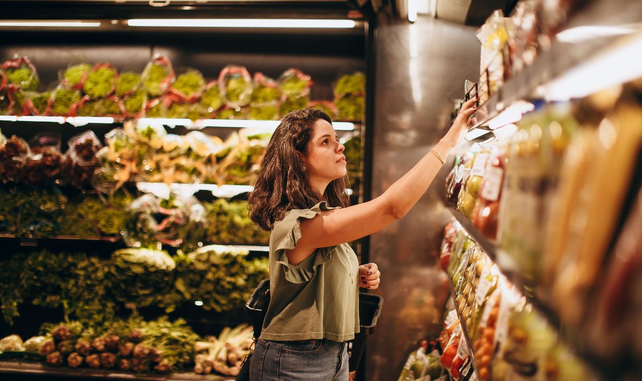 A woman selects fresh vegetables in a well-lit supermarket
