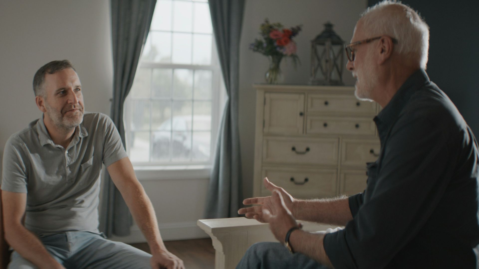 Two men talking in a sunlit room