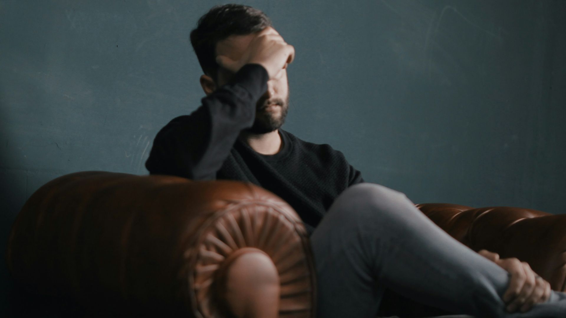 a man holds his head while sitting on a sofa