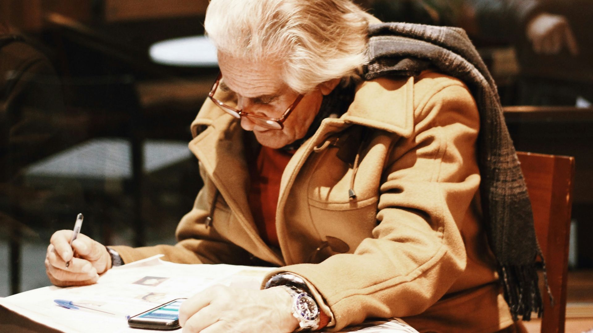 man in brown coat writing on white paper